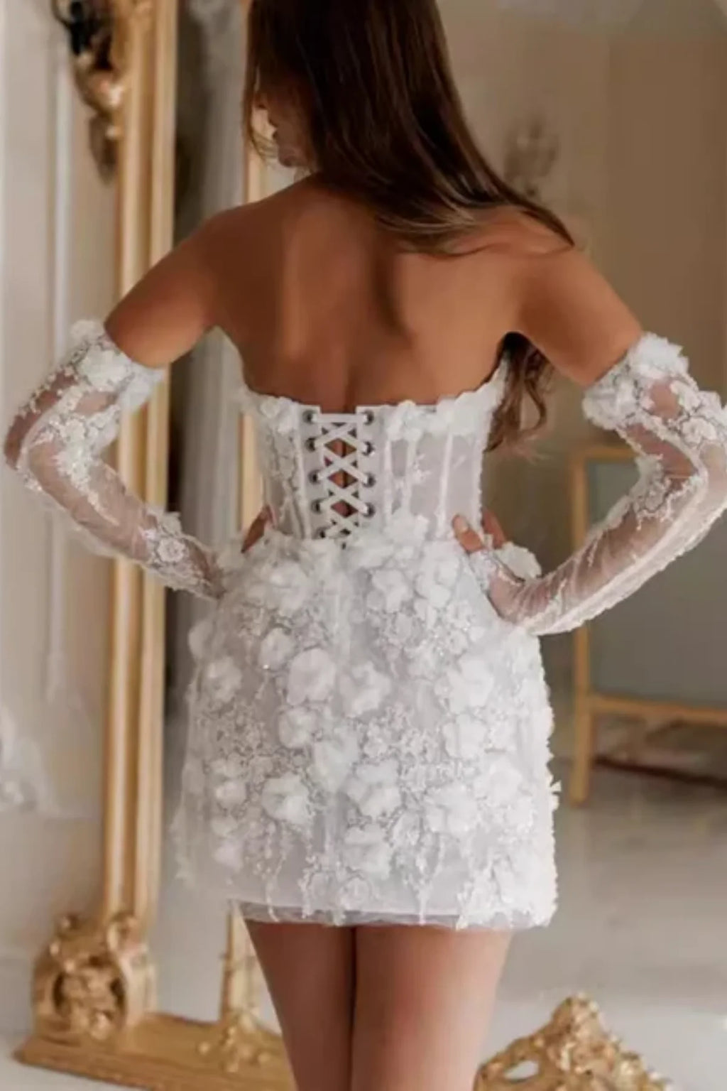 Back view of a short white bridal shower dress featuring an exposed boning corset bodice with a lace-up closure, covered in 3D floral appliqués and paired with detached lace sleeves