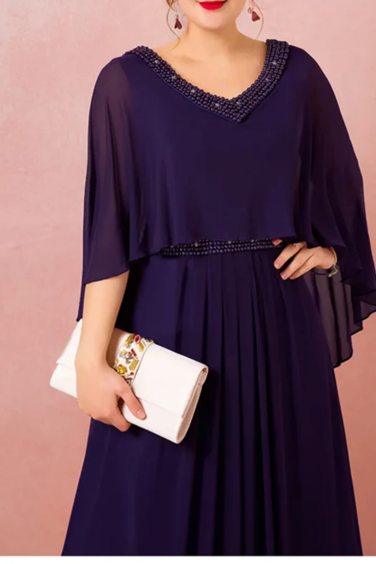 Close-up front view of navy blue mother of the bride dress with beaded neckline, sheer chiffon cape sleeves, and flowing A-line skirt, styled with a clutch bag