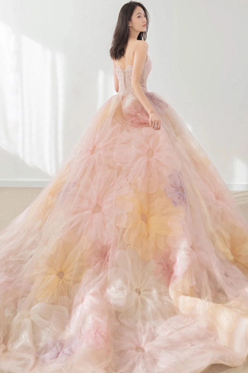 Back view of a model showcasing a strapless pink floral bridal gown with a lace-up corset back and a dramatic, sweeping cathedral train