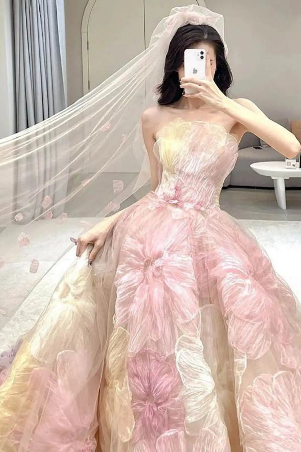 Close-up of the strapless bodice of a pink floral bridal gown, paired with a sheer tulle wedding veil delicately scattered with matching pink petals