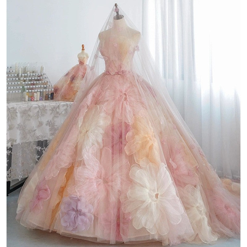 Studio display of a luxury pink and multi-colored organza flower wedding dress on a mannequin, showing the full volume of the pleated tulle skirt