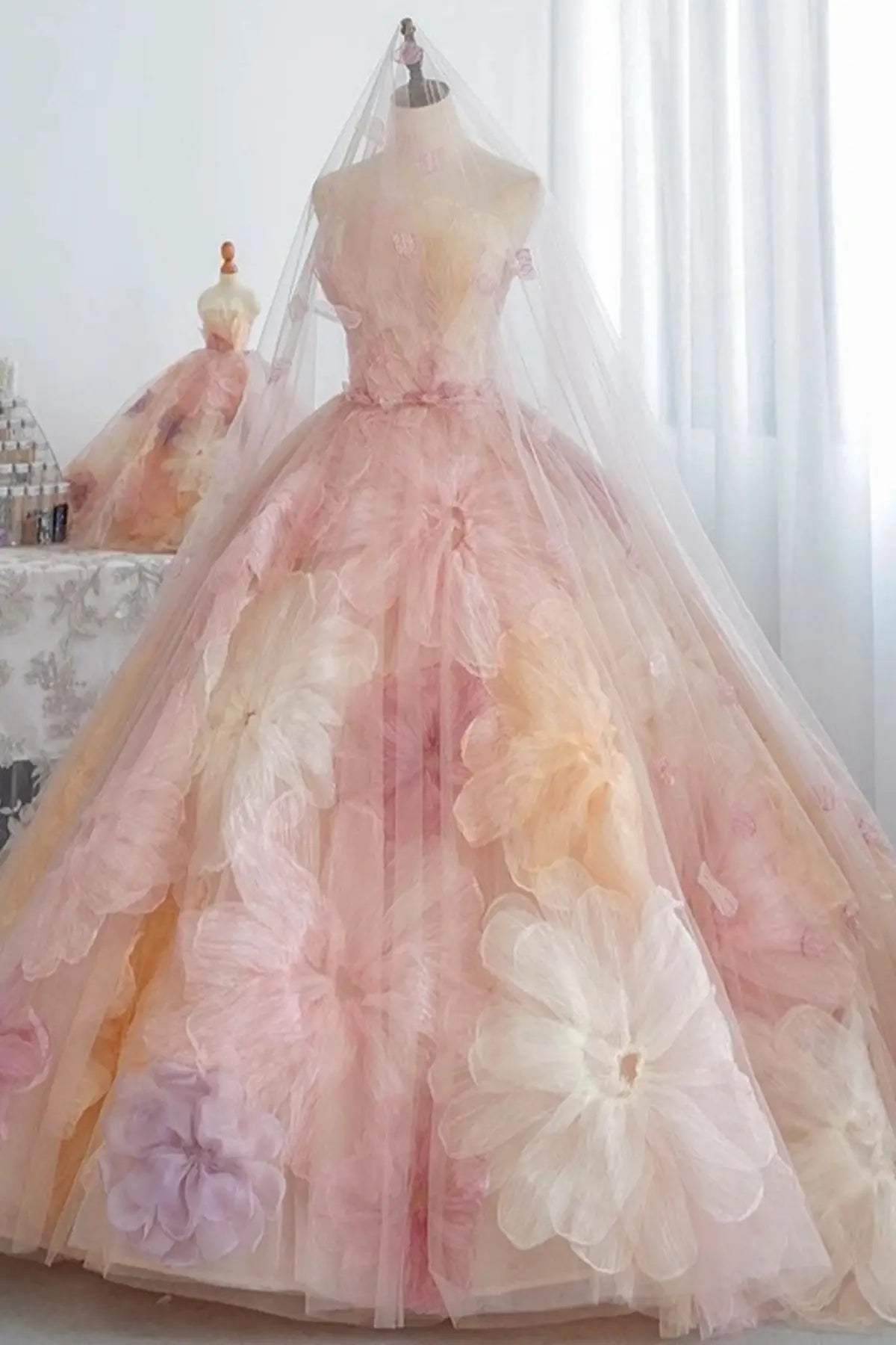 Close-up of a designer adjusting a sheer tulle bridal veil detailed with floating pink organza petals over a textured floral bodice