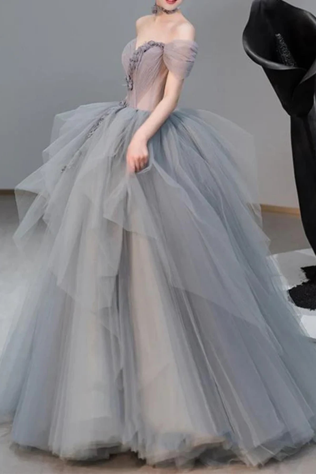 Side view of a model posing in a flowing silver-grey tulle wedding dress, highlighting the soft, unstructured layers of the floor-length skirt.