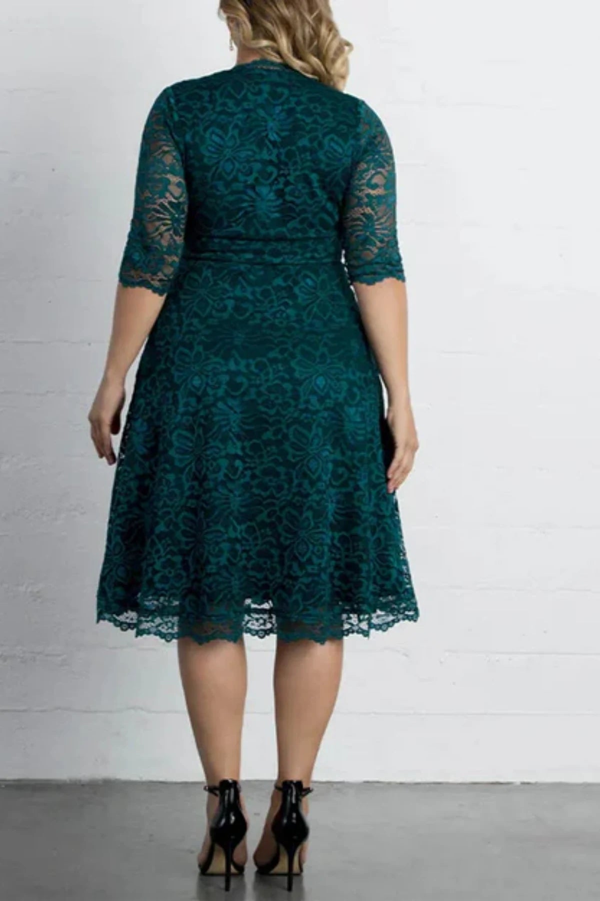 Full back view of an emerald green lace cocktail dress, showing a high zipped back design, sheer lace sleeves, and a straight knee-length hemline