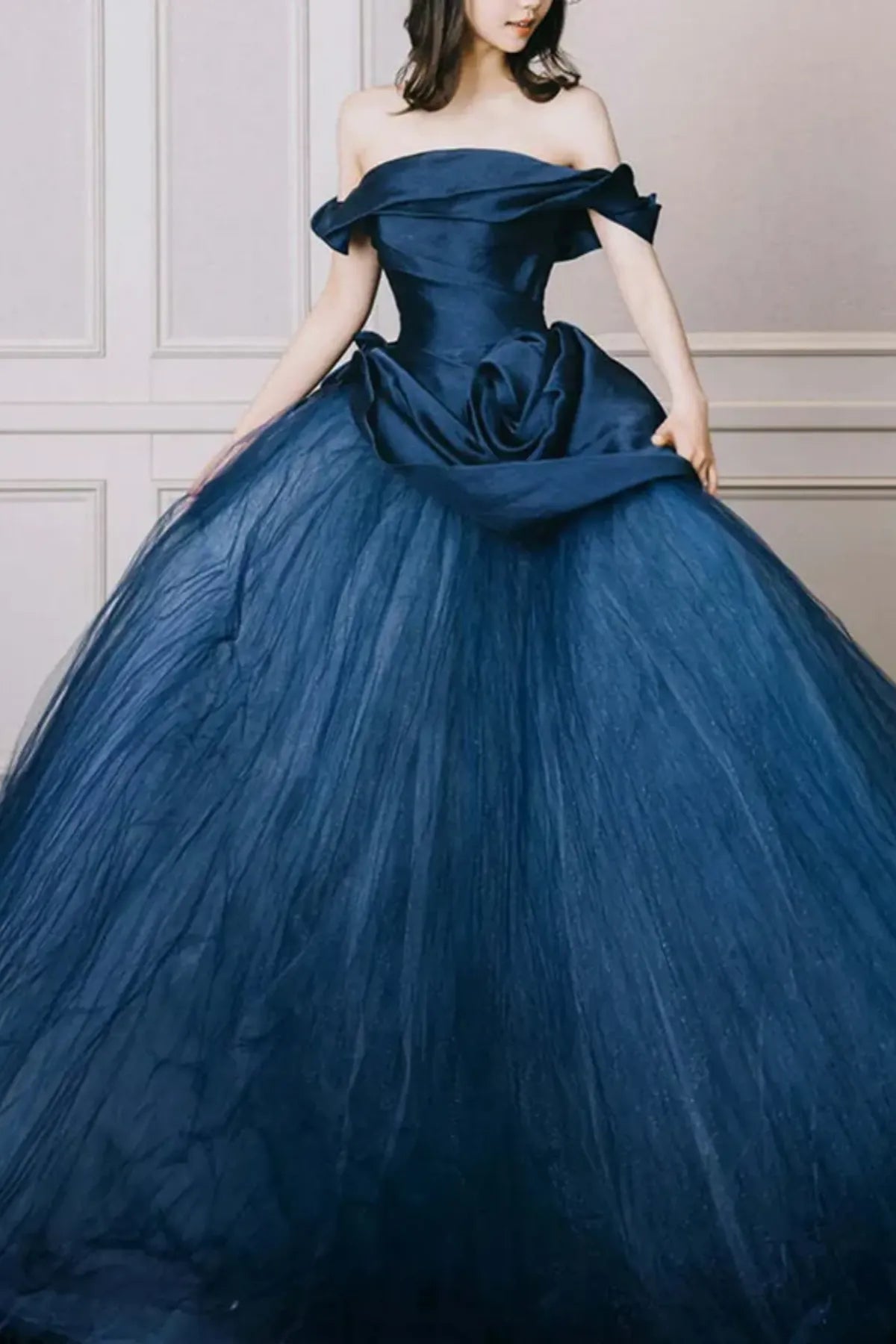 Front view of an off-the-shoulder midnight navy blue bridal ballgown featuring a structured satin bodice and a voluminous tulle skirt with a large ruched fabric rosette at the waist