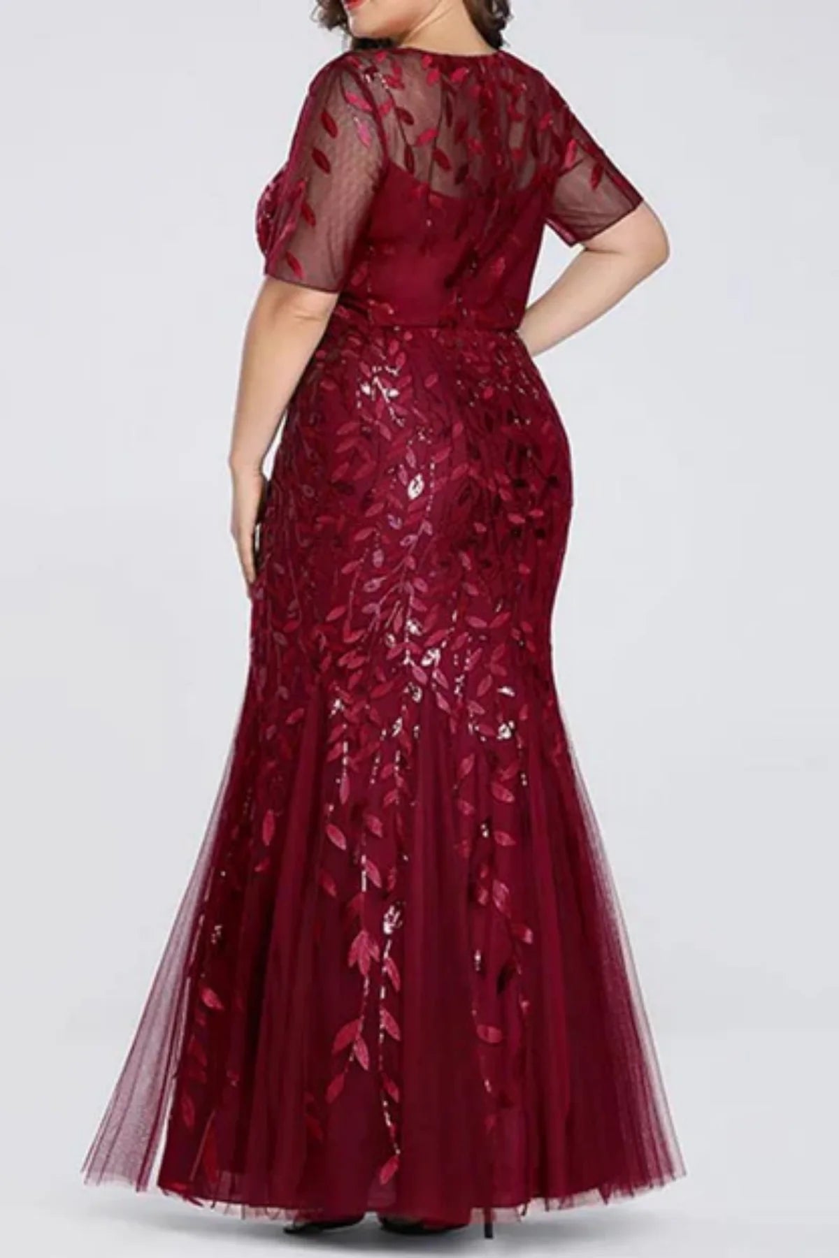Back view of a burgundy mermaid evening gown on a mannequin, featuring sheer illusion long sleeves, a V-neckline, and cascading metallic leaf embroidered appliqués