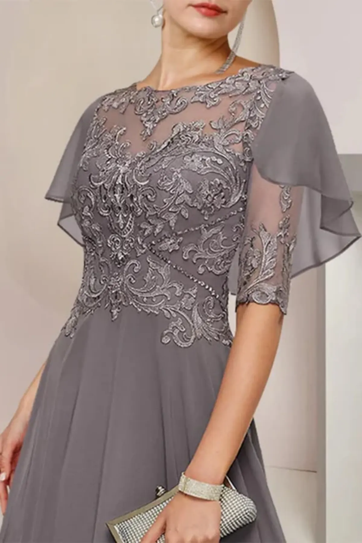 Close-up of the bodice on a navy blue formal evening gown, highlighting the sheer elbow-length cape overlay covered in intricate floral embroidery