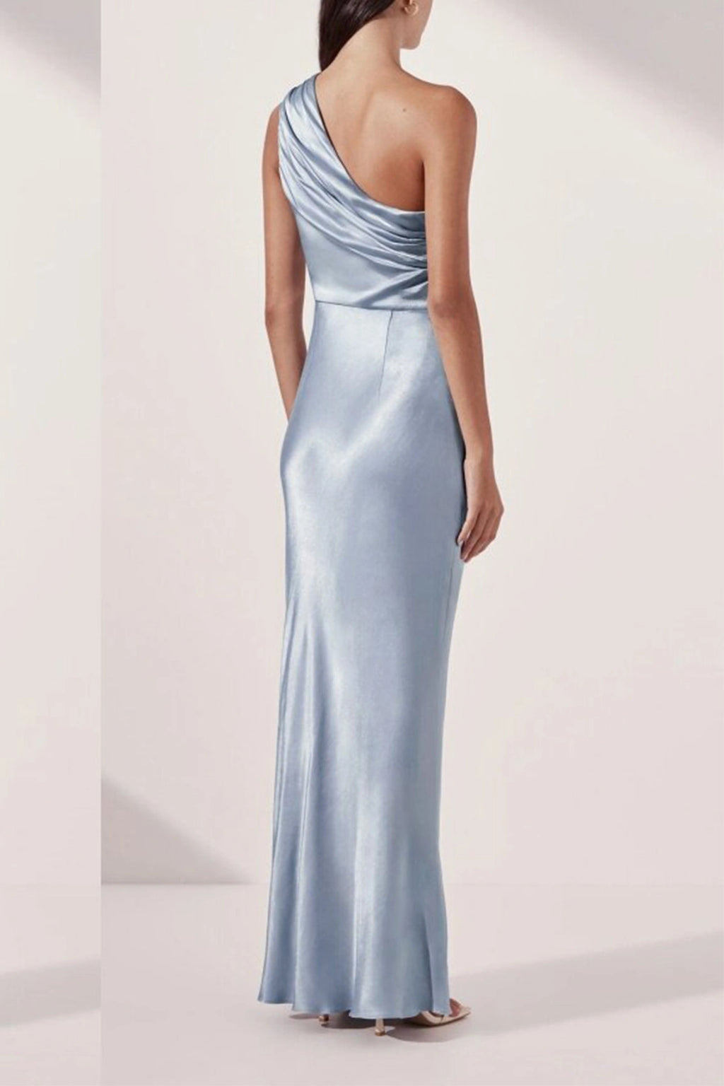 Back view of a light blue satin one-shoulder evening dress showcasing asymmetric back pleating and a sleek fitted waist.