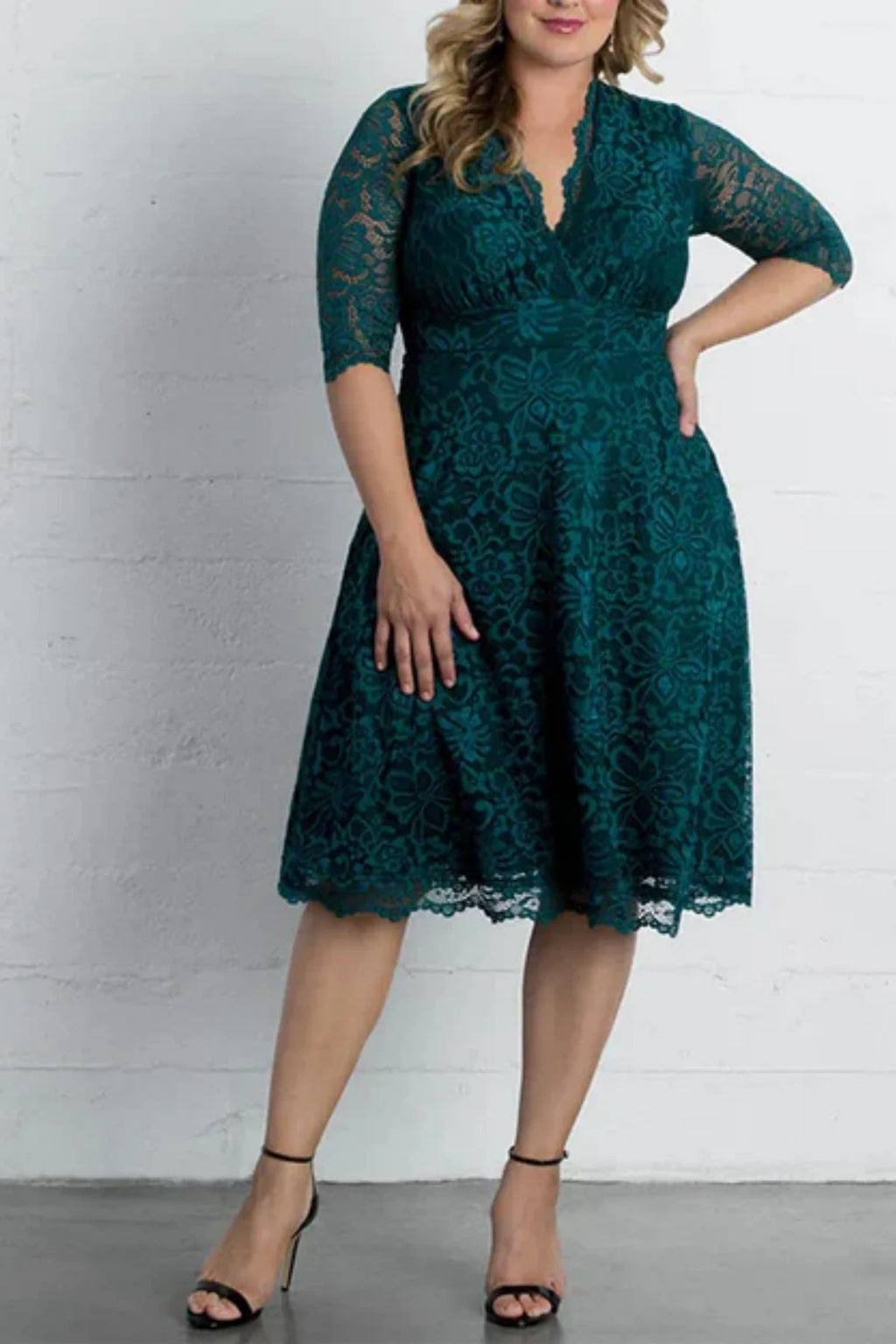 Full-length front view of an emerald green knee-length mother of the bride dress, featuring a V-neckline, elbow sleeves, and a beaded satin belt