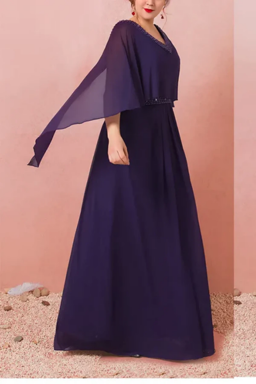 Side  of navy chiffon mother of the bride gown with beaded waist detail, flowing cape sleeves, and soft pleated skirt in motion