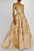 Close-up of the bodice on a champagne gold formal gown, displaying a structured off-the-shoulder neckline, mid-length sleeves, and detailed gold vine and feather embroidery