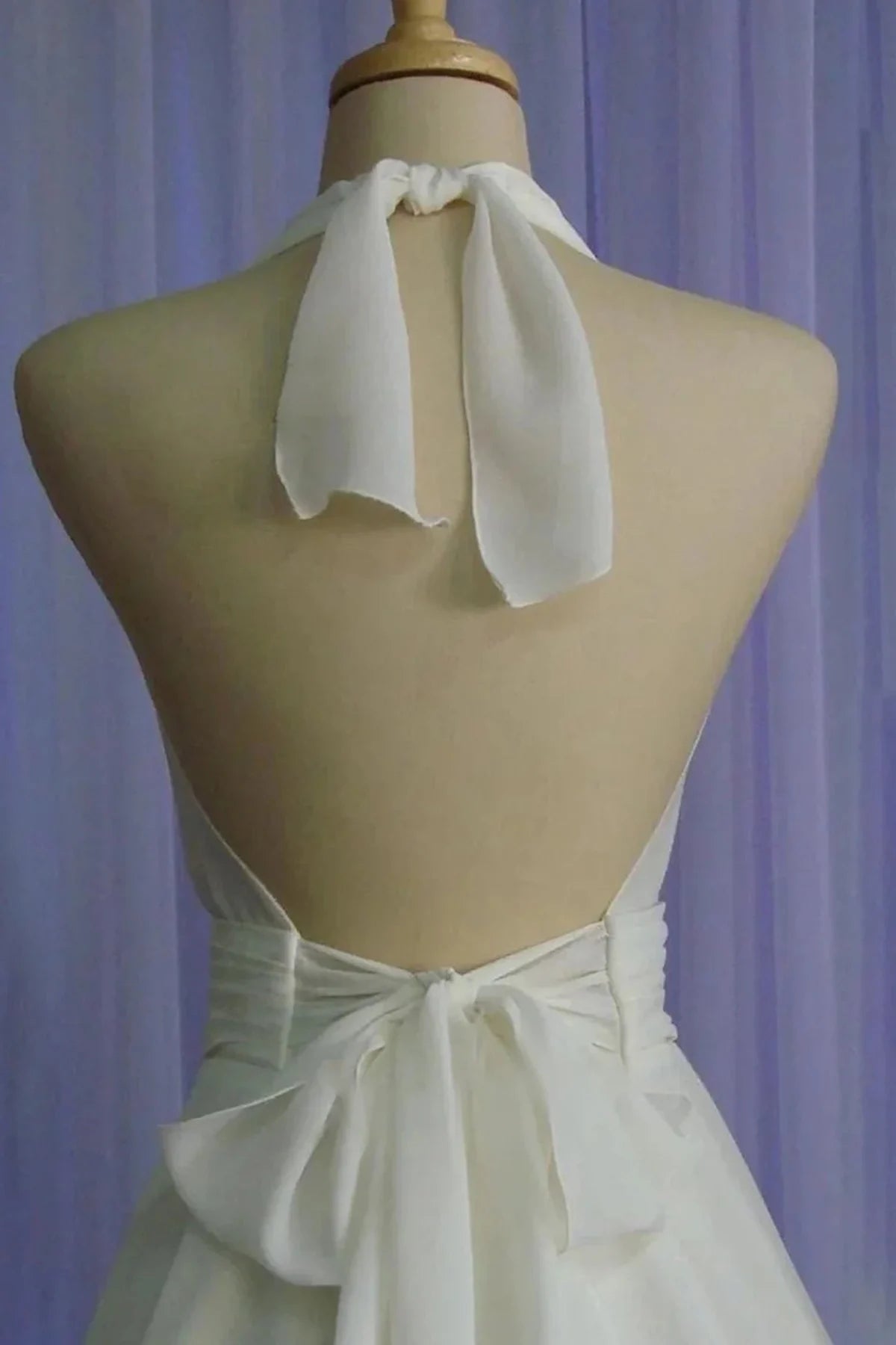 Close-up of the back of a chiffon dress on a mannequin, showing the soft fabric ties at the neck and the matching bow at the lower back