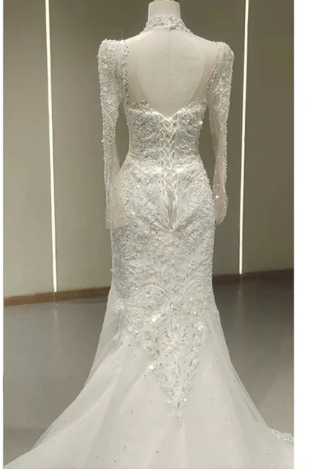 ack view of a white trumpet wedding dress featuring an intricate corset lace-up closure, a high sheer neck, and heavy sequin and bead embellishments