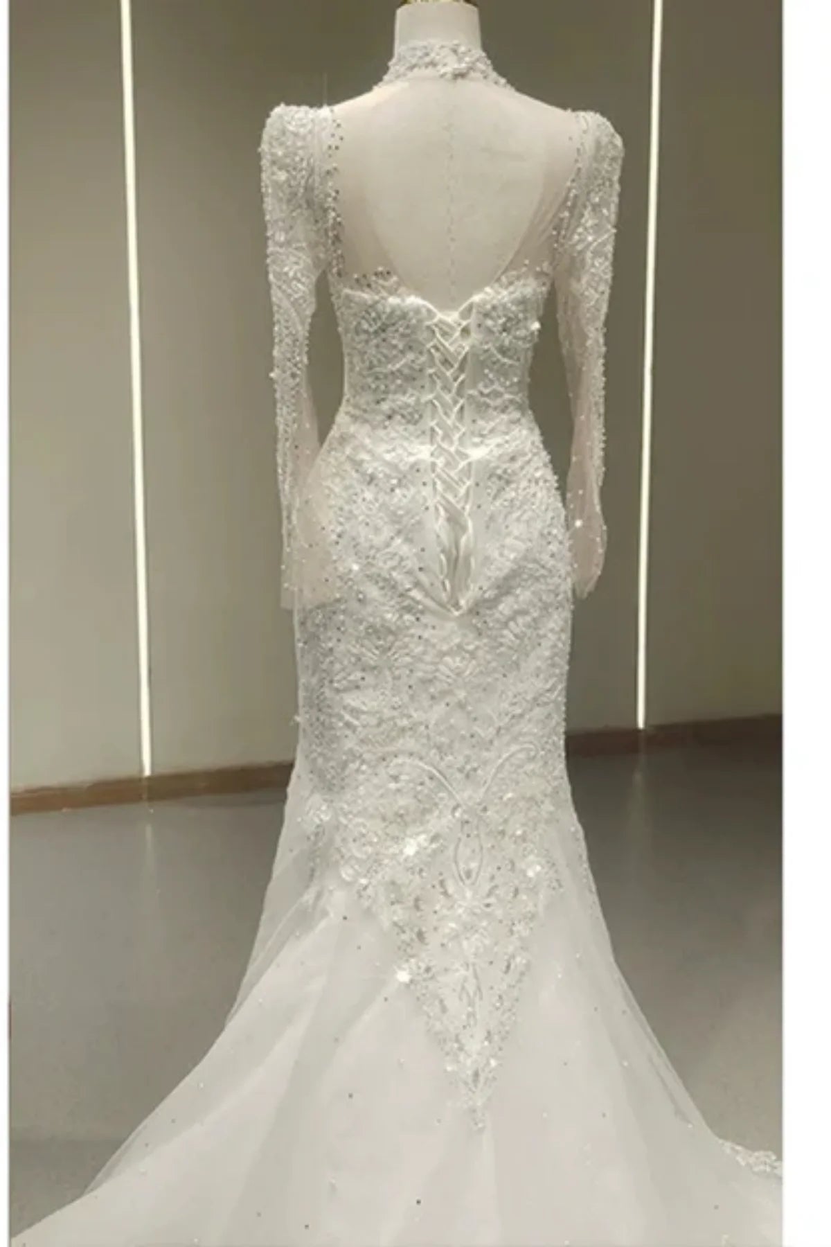 ack view of a white trumpet wedding dress featuring an intricate corset lace-up closure, a high sheer neck, and heavy sequin and bead embellishments