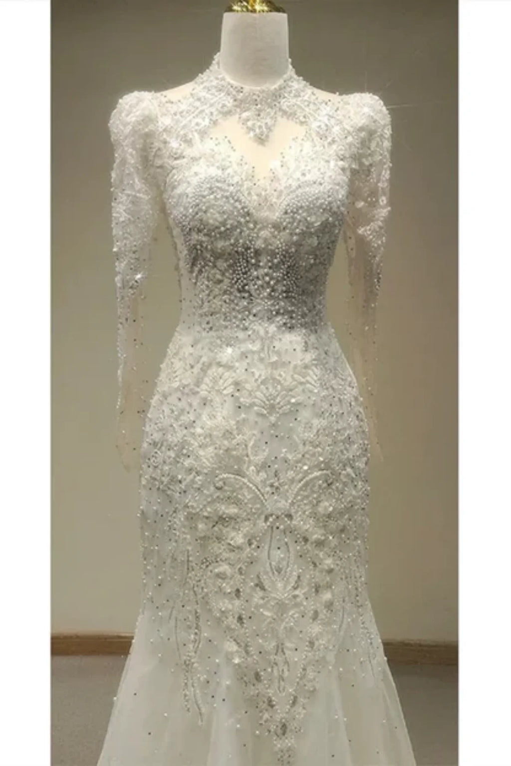 Close-up of the front of a white bridal gown showcasing a high illusion neckline, structured shoulders, and elaborate floral beadwork and crystals