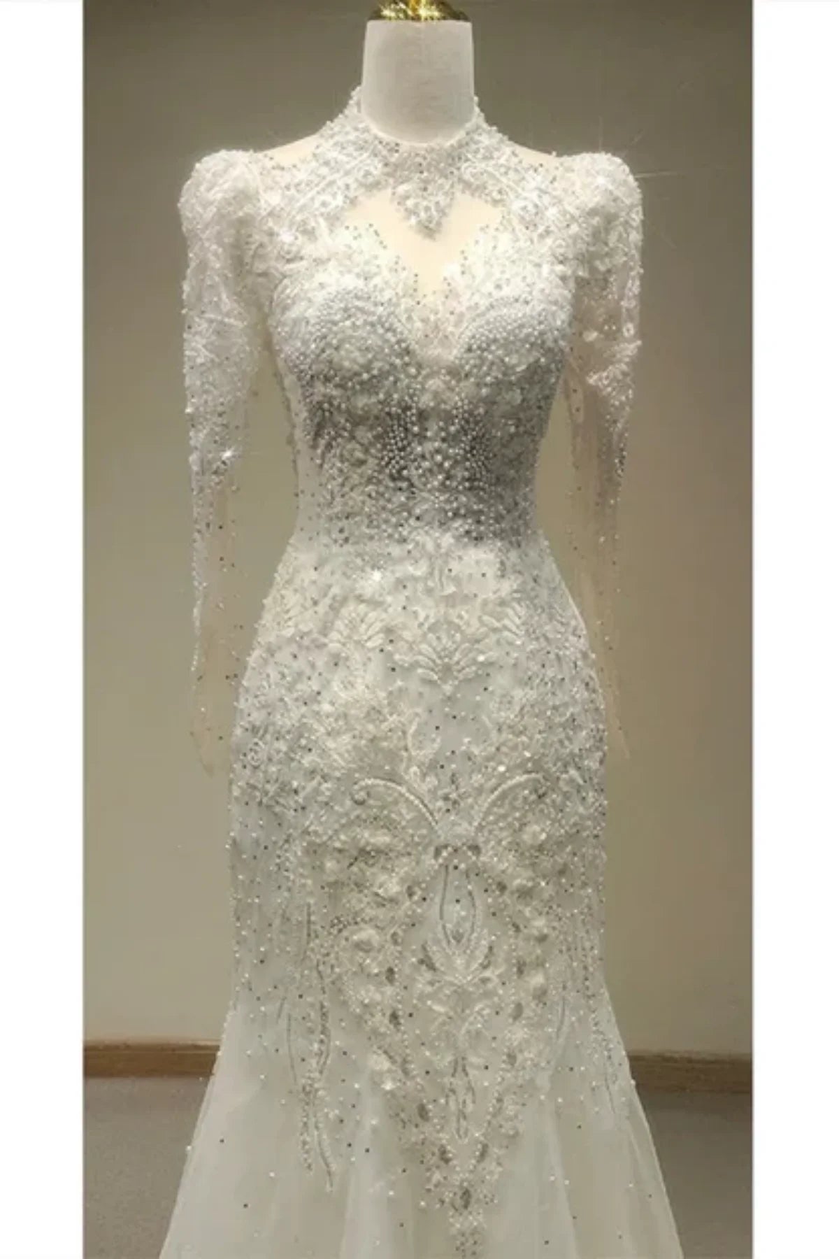 Close-up of the front of a white bridal gown showcasing a high illusion neckline, structured shoulders, and elaborate floral beadwork and crystals