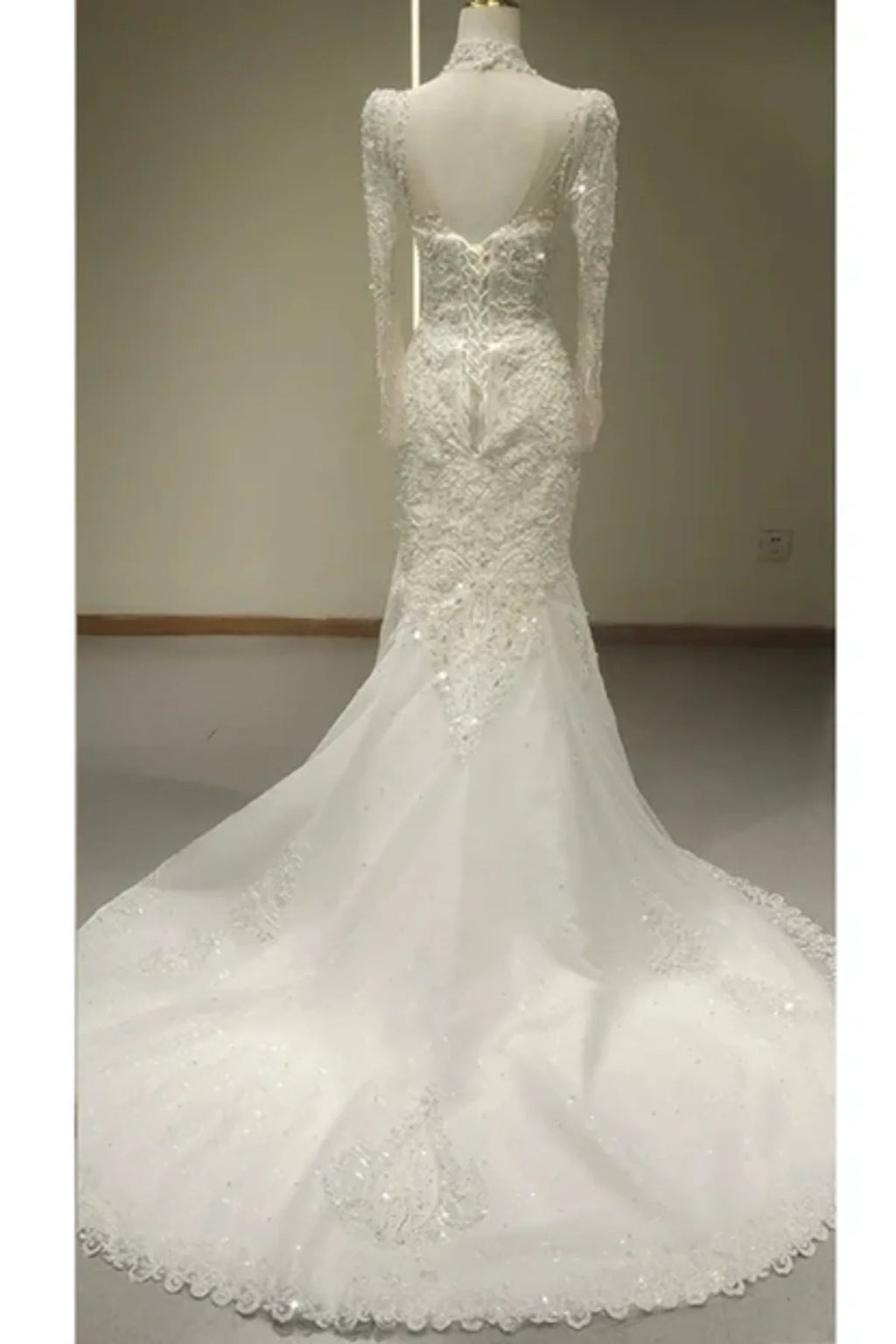 Full back view of a long-sleeve mermaid wedding dress on a mannequin, displaying a dramatic chapel-length tulle train with lace borders