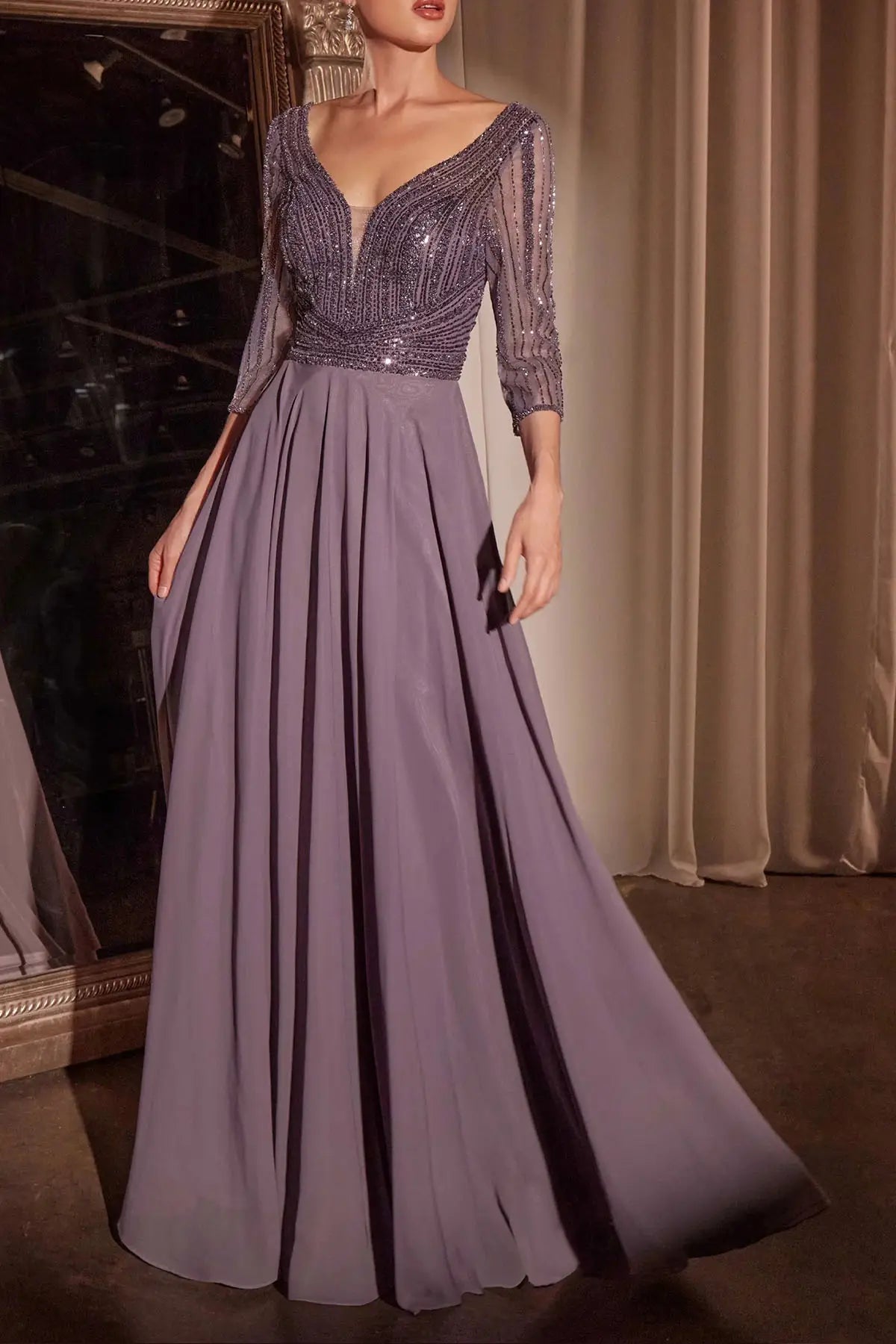 A floor-length formal gown in dusty lavender-purple, featuring a heavily beaded and sequined V-neck bodice with three-quarter sheer sleeves and a flowing chiffon skirt, shown on a model in an indoor setting.