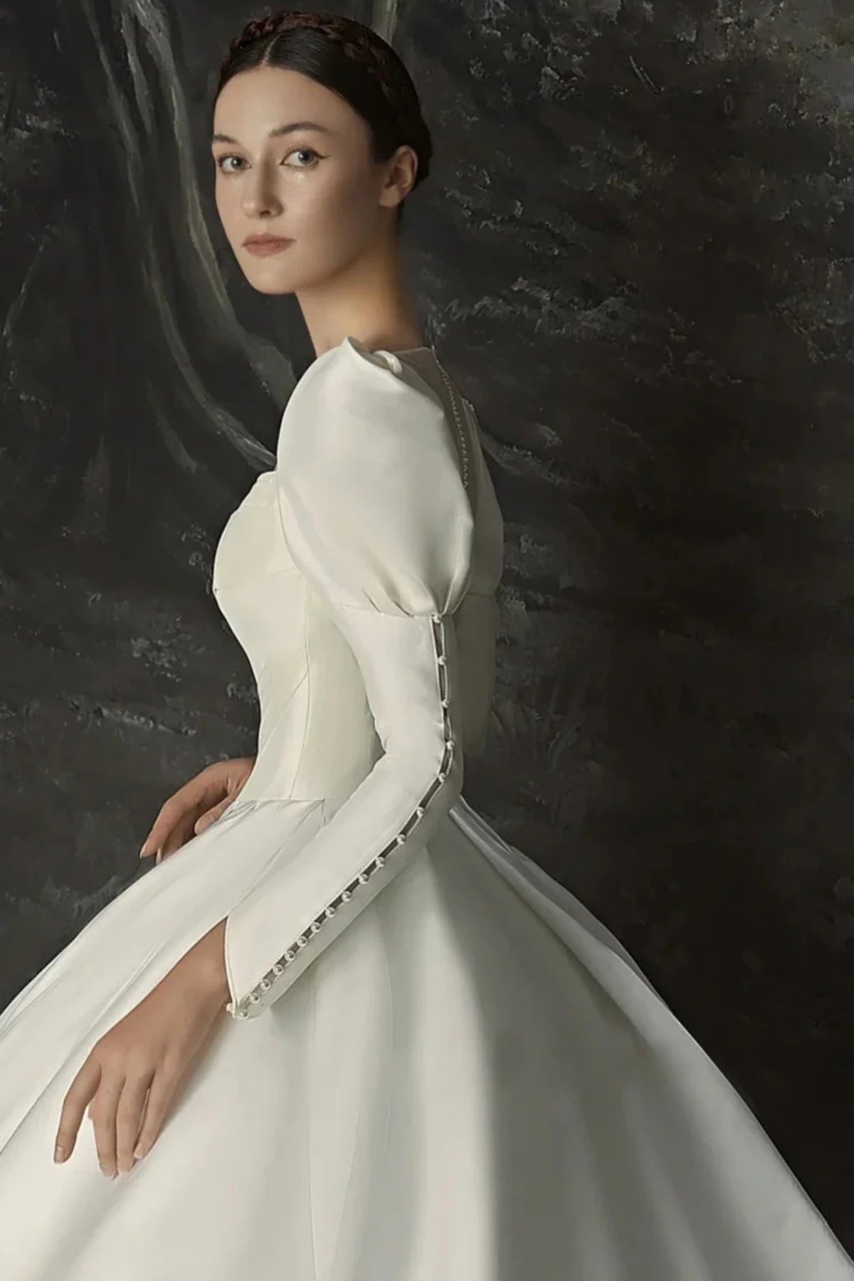 Minimalist satin bridal gown with structured bodice and long puff sleeves shown in side portrait view