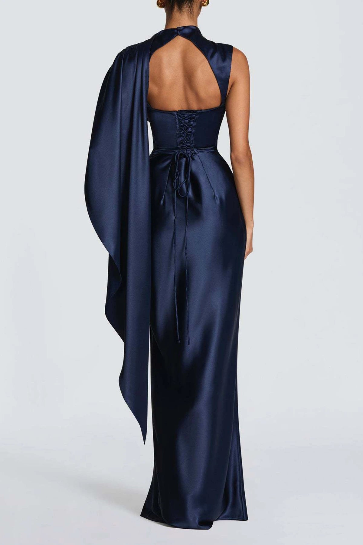 Back view of a navy blue satin formal gown featuring an open back, lace-up bodice, and long draped cape