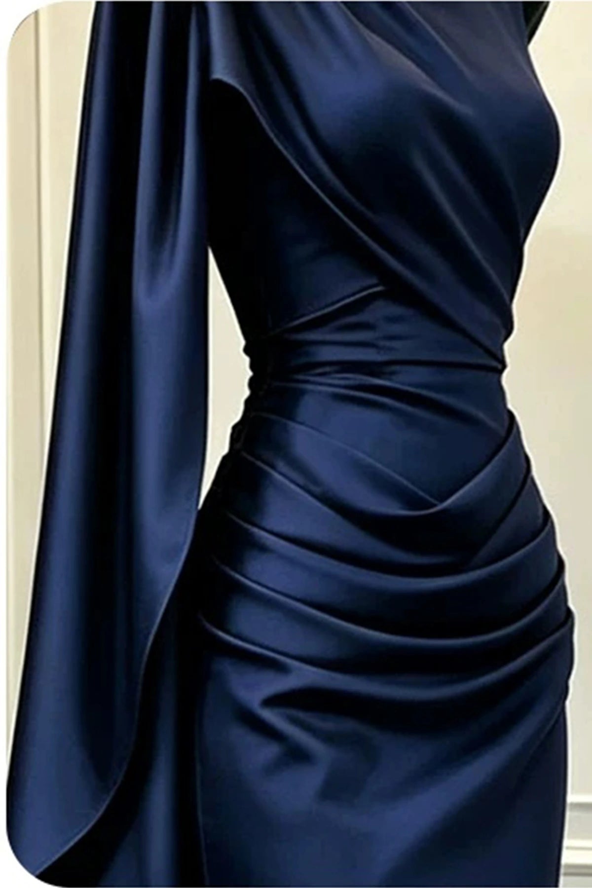 Close-up of the cowl high neckline, cinched waist pleats, and cascading side sleeve on a navy satin formal gown