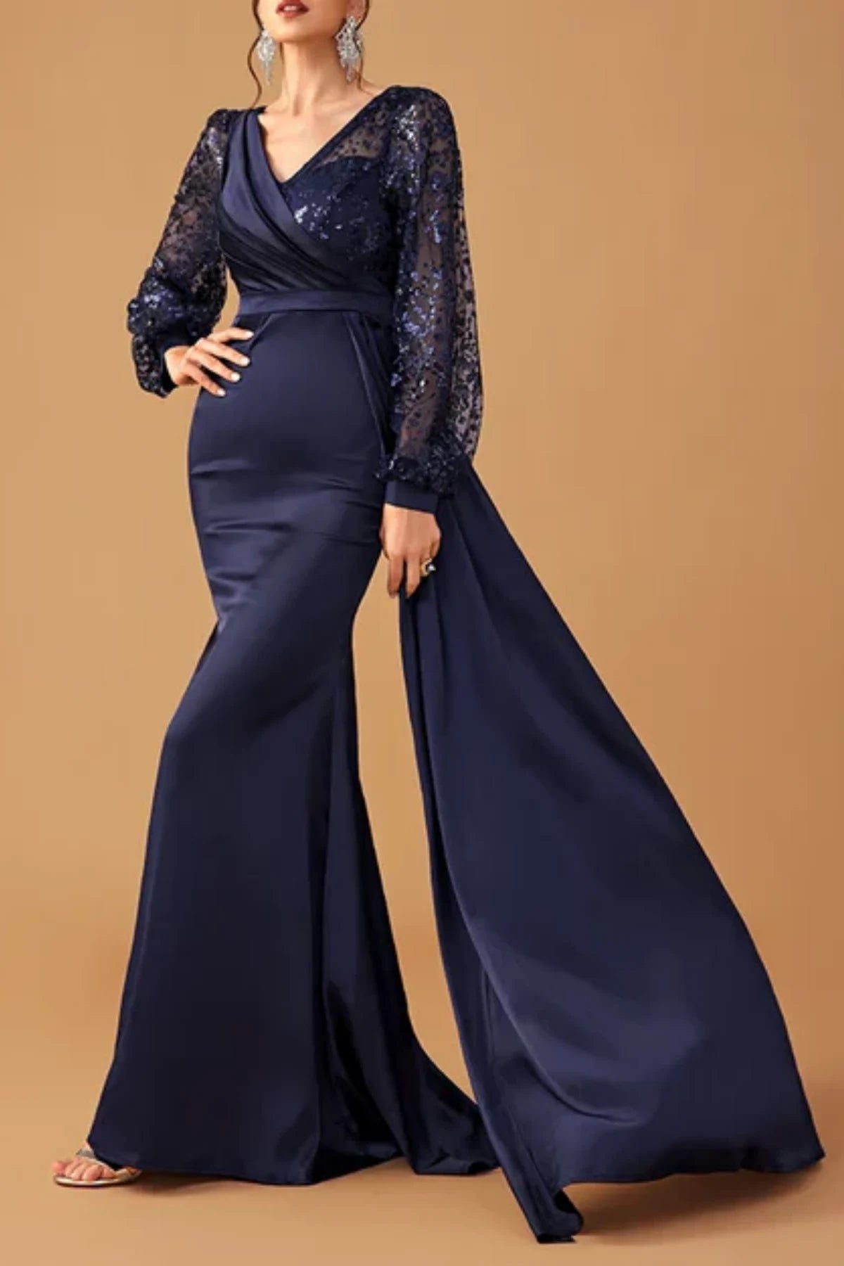 Angled front view of a dark navy blue satin formal trumpet dress on a mannequin, highlighting the flared lower skirt and sculptural sleeve ruffles
