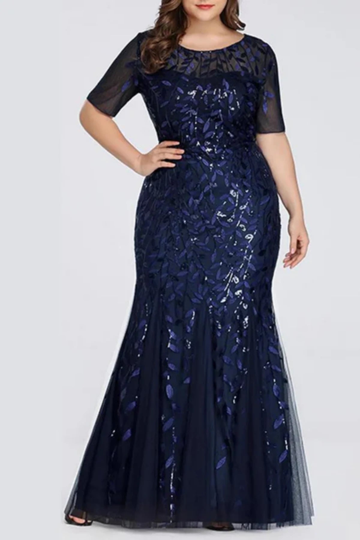 Front view of a navy blue formal trumpet gown featuring intricate silver leaf appliqués over a sheer illusion bodice and long sleeves