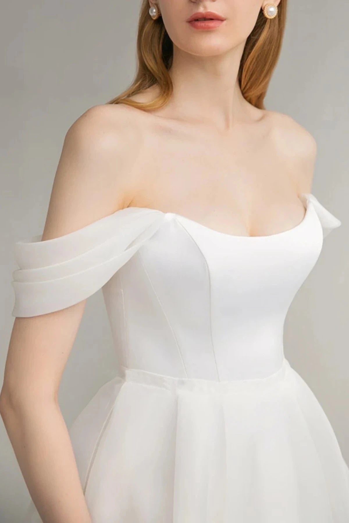 Full front view of a model wearing an ivory off-the-shoulder midi A-line bridal dress with nude heels