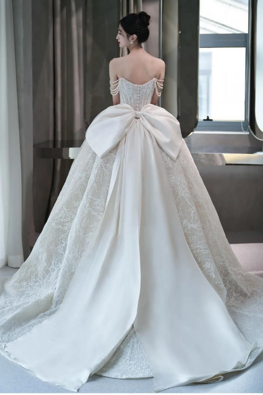 Back full-length view of an embroidered champagne bridal gown highlighting a romantic low-back design and a soft tulle sweep train