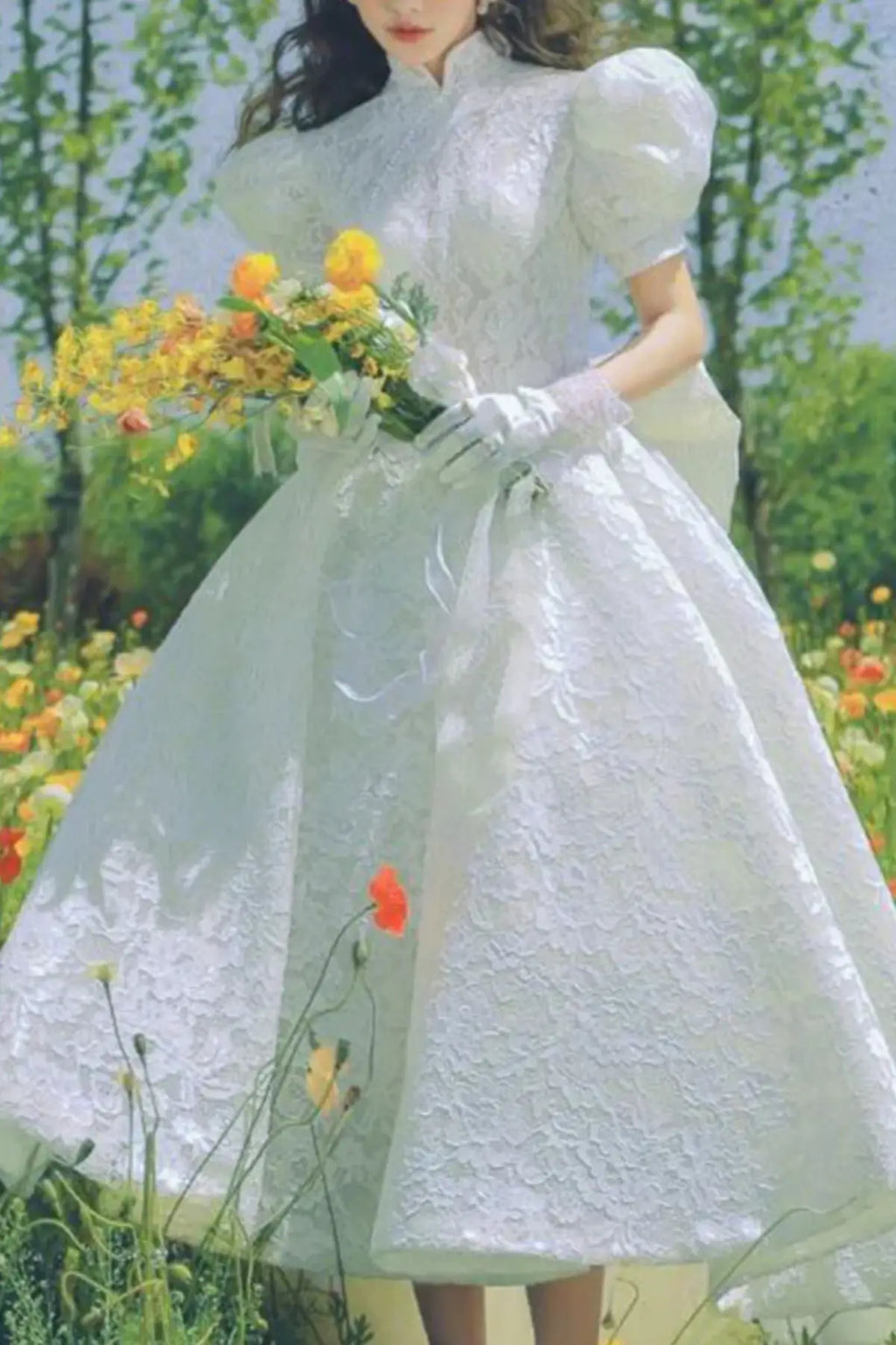 Romantic lace bridal dress with high neckline, puff sleeves and tea-length skirt in a flower garden