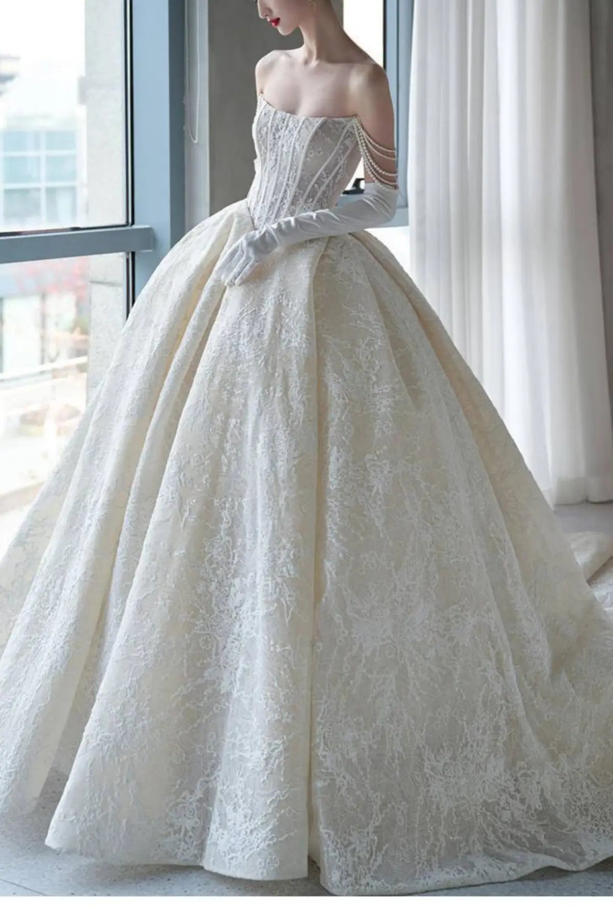Side view of a model wearing a champagne lace wedding dress, highlighting the romantic draped off-the-shoulder sheer sleeves and delicate floral trailings
