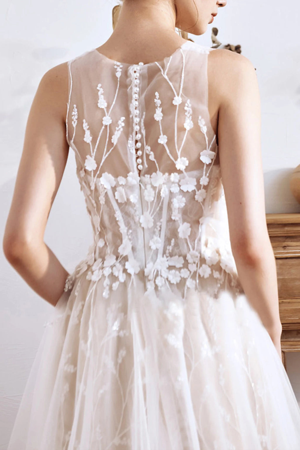 Close-up of a sheer illusion back wedding dress featuring covered buttons and delicate floral vine embroidery