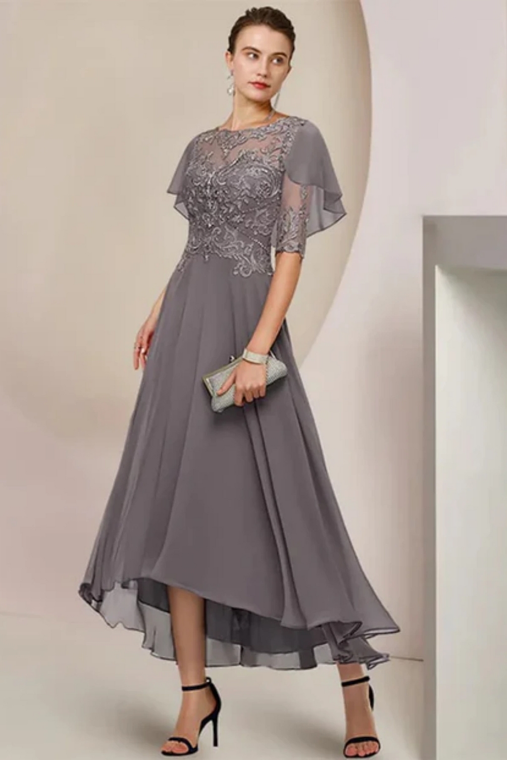 Full-length front view of a slate grey mother of the groom dress on a mannequin, featuring a fit-and-flare skirt and a sheer attached capelet with matching floral lace appliqués