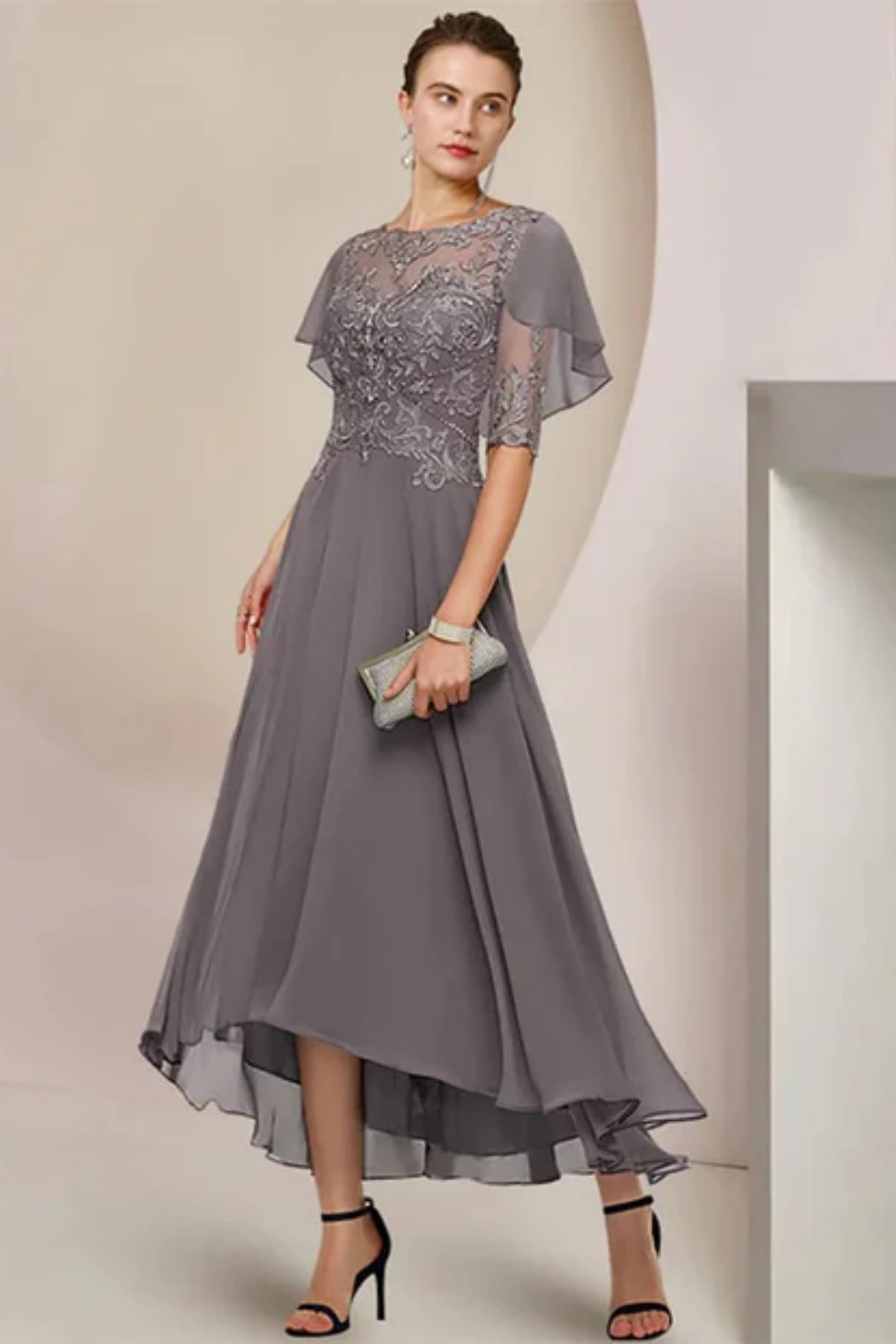 Full-length front view of a slate grey mother of the groom dress on a mannequin, featuring a fit-and-flare skirt and a sheer attached capelet with matching floral lace appliqués