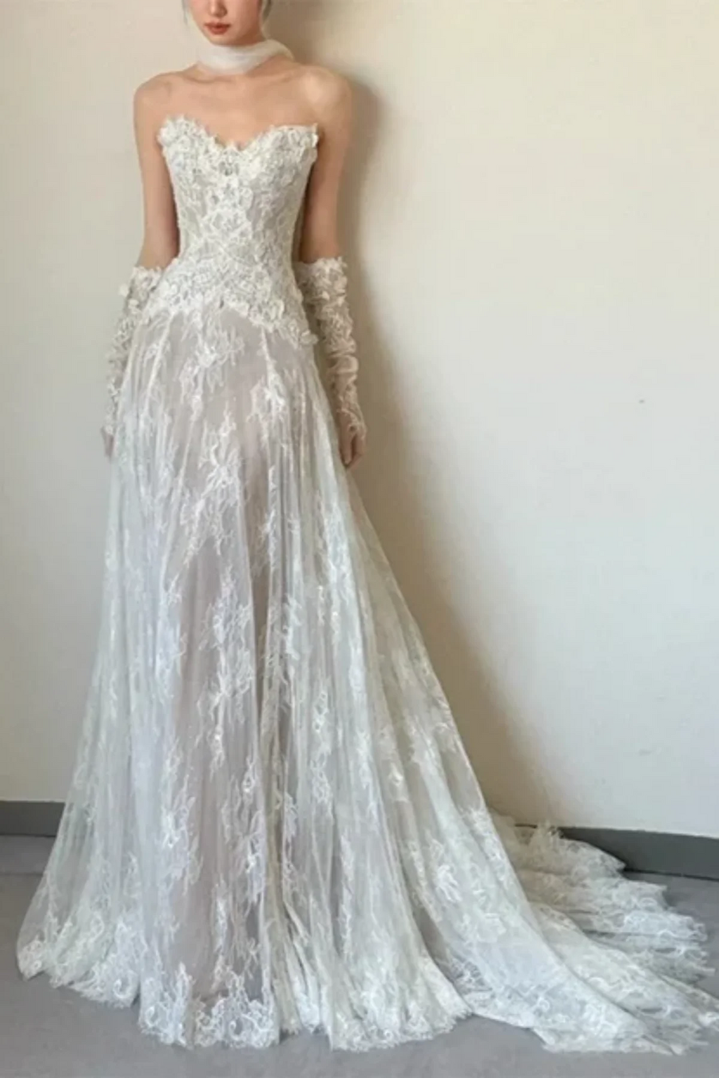 Model wearing an ivory A-line lace wedding dress with a strapless sweetheart neckline, paired with a sheer tulle neck scarf and matching opera-length lace gloves