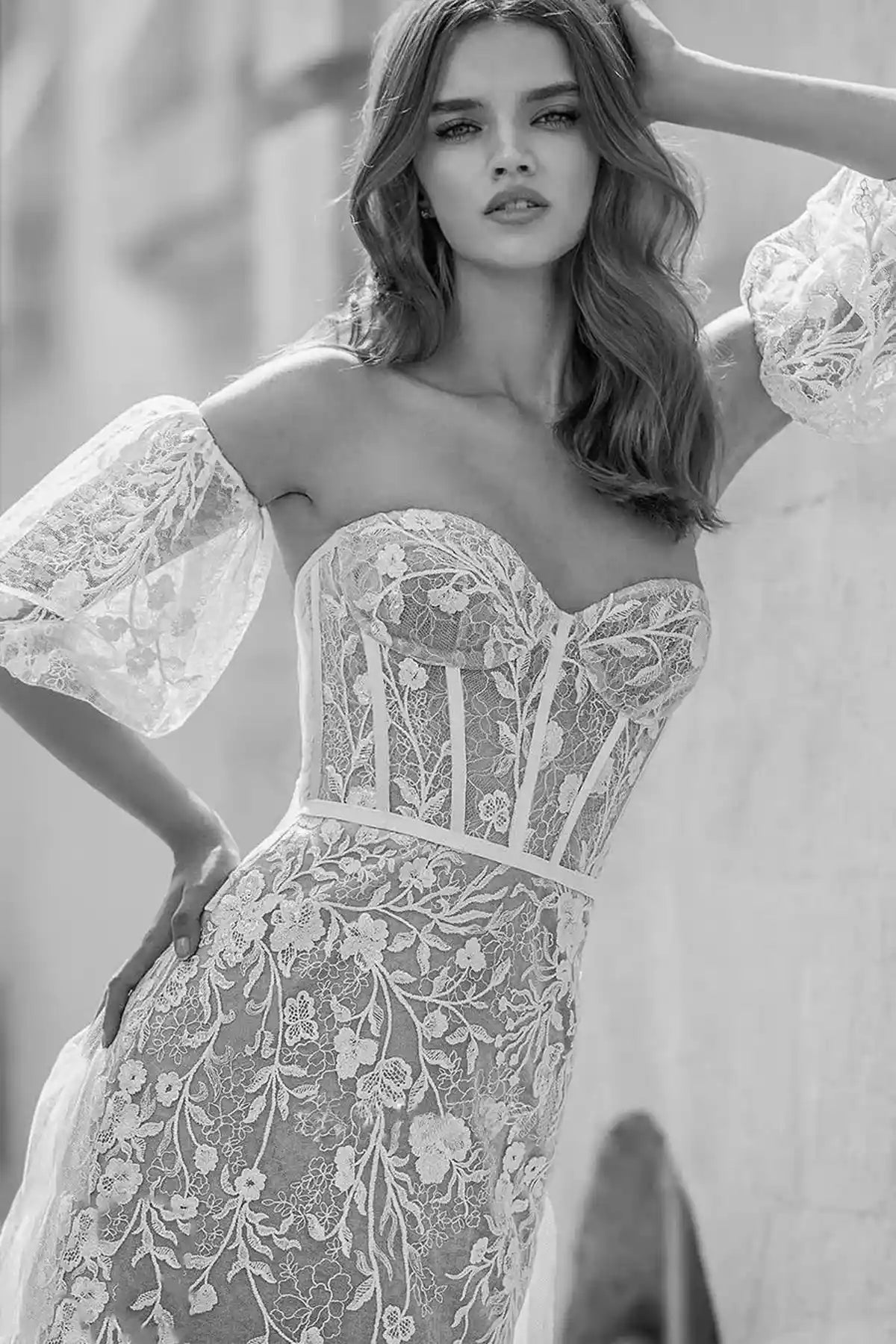 front full-length view of a model in a nude illusion mermaid wedding dress featuring white floral lace overlays and voluminous off-the-shoulder puff sleeves