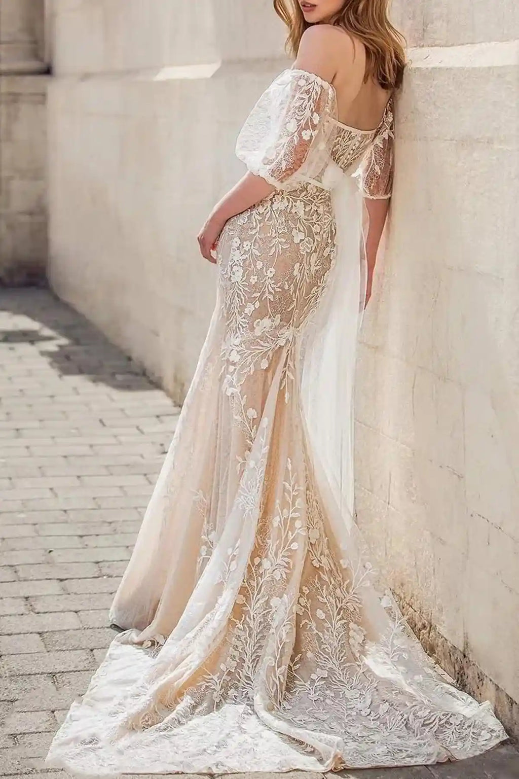 Rear view of the mermaid bridal gown highlighting a low-cut corset back, intricate lace patterns along the train, and oversized sheer tulle accent bows