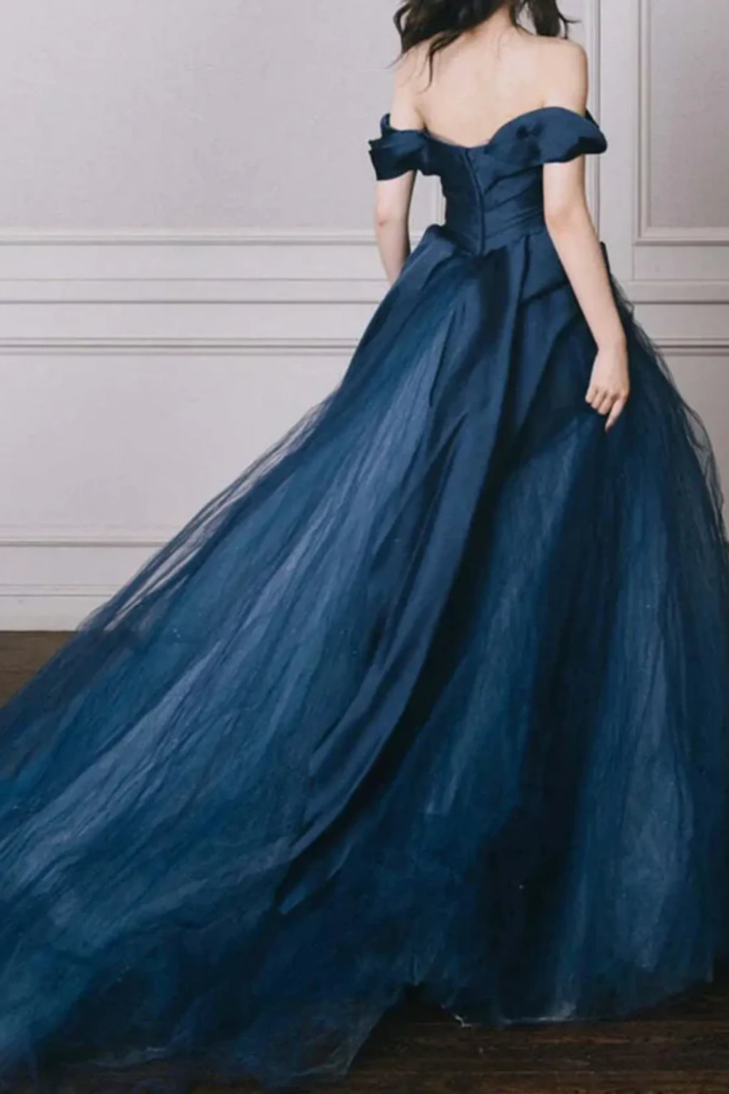 Back view of a modern navy blue bridal gown showing the off-the-shoulder sleeve details, a structured corset-style back, and a flowing tulle sweep train