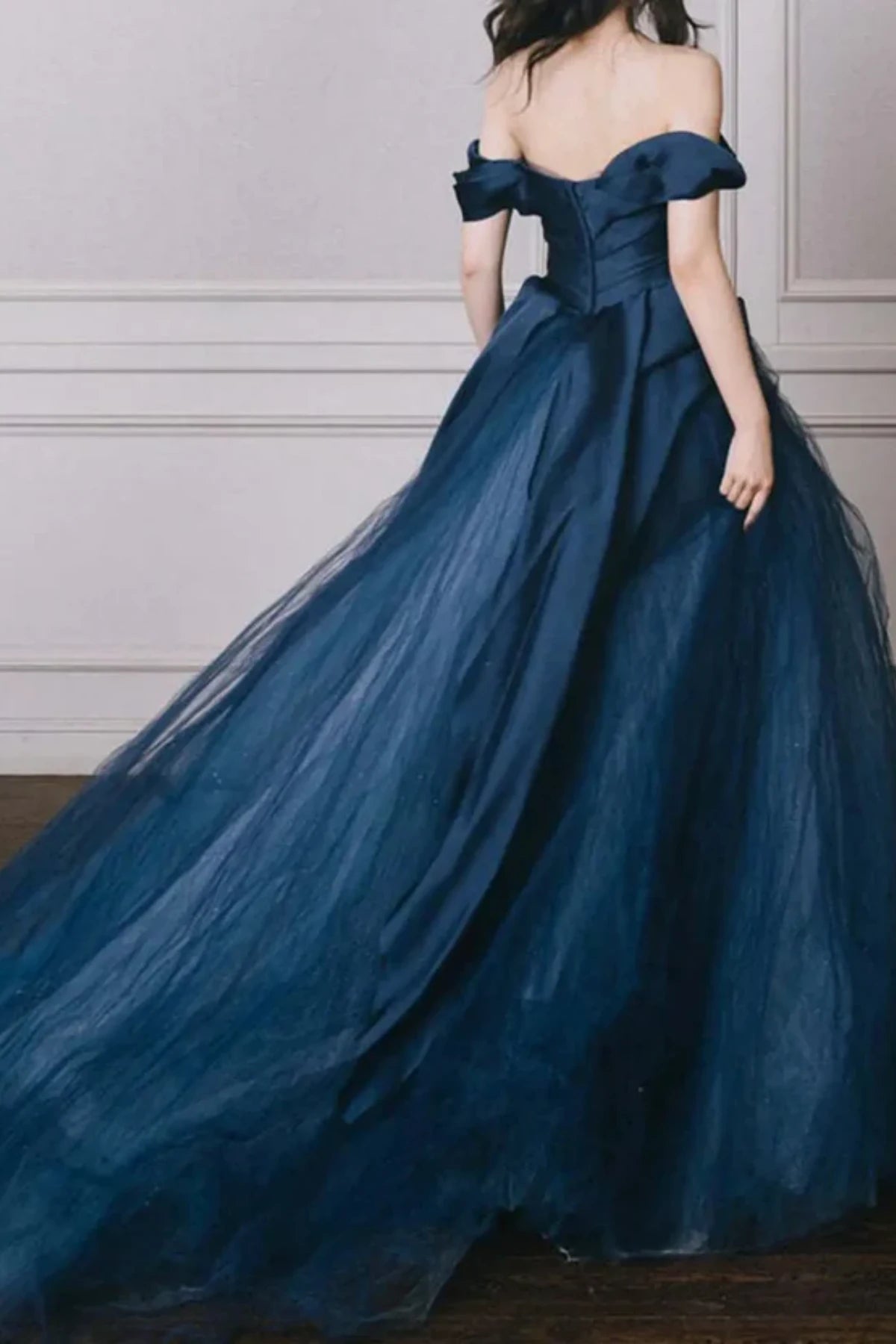 Back view of a modern navy blue bridal gown showing the off-the-shoulder sleeve details, a structured corset-style back, and a flowing tulle sweep train