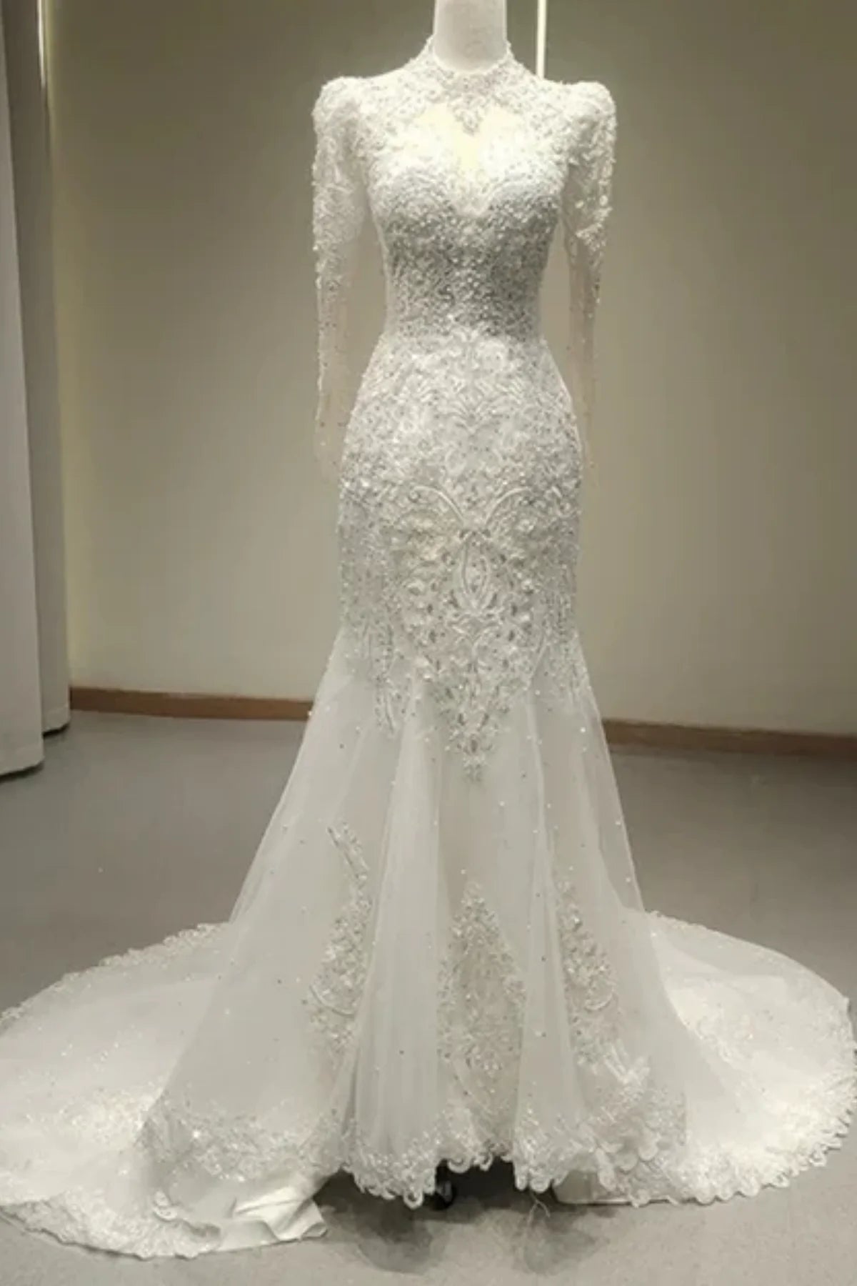 Full-length front view of a heavily beaded white mermaid wedding dress with long sleeves, a high collar, and a flared tulle skirt